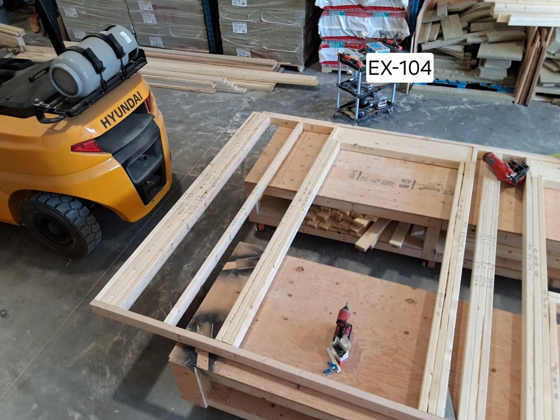 Timber-framed components laid out beside a yellow forklift on a factory floor.
