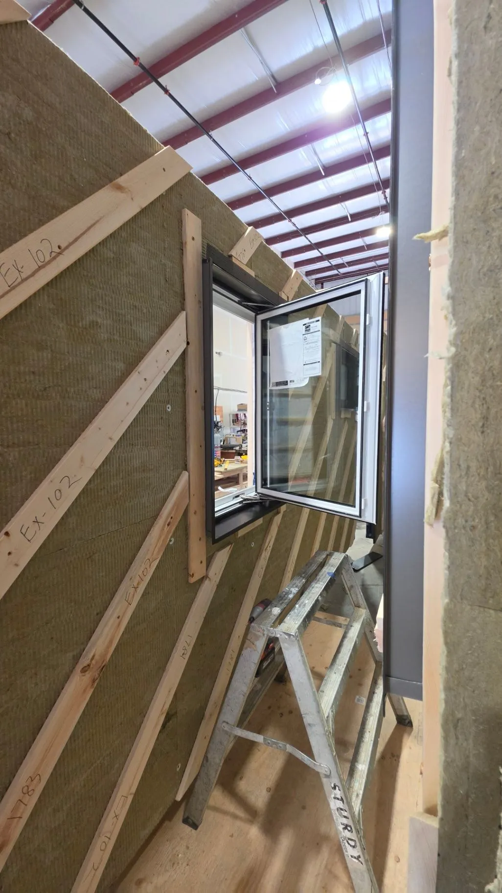 An open window in a timber wall assembly inside the factory, with insulation visible along the edge.
