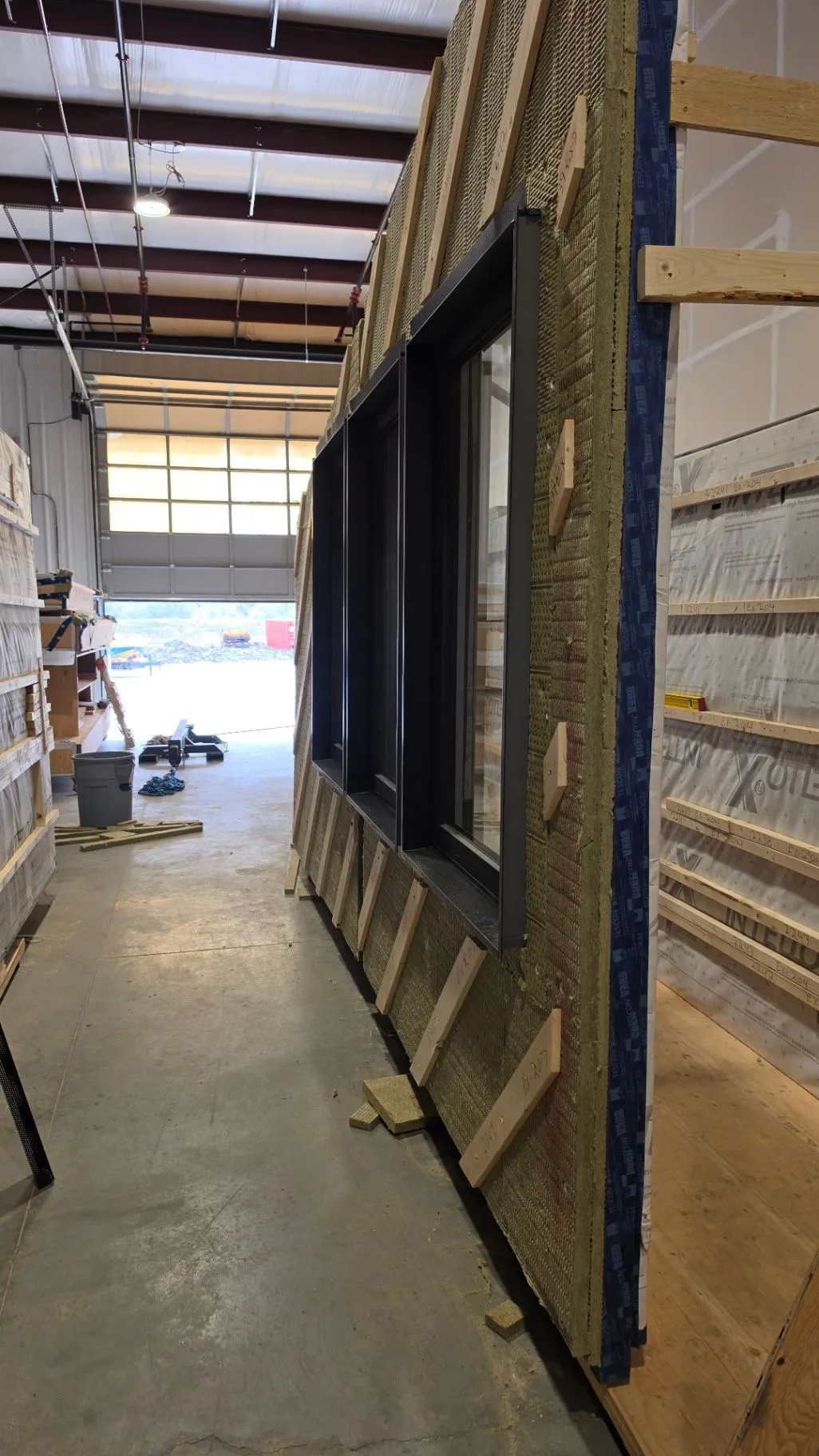 A factory wall assembly with exposed insulation and an installed dark-framed window.