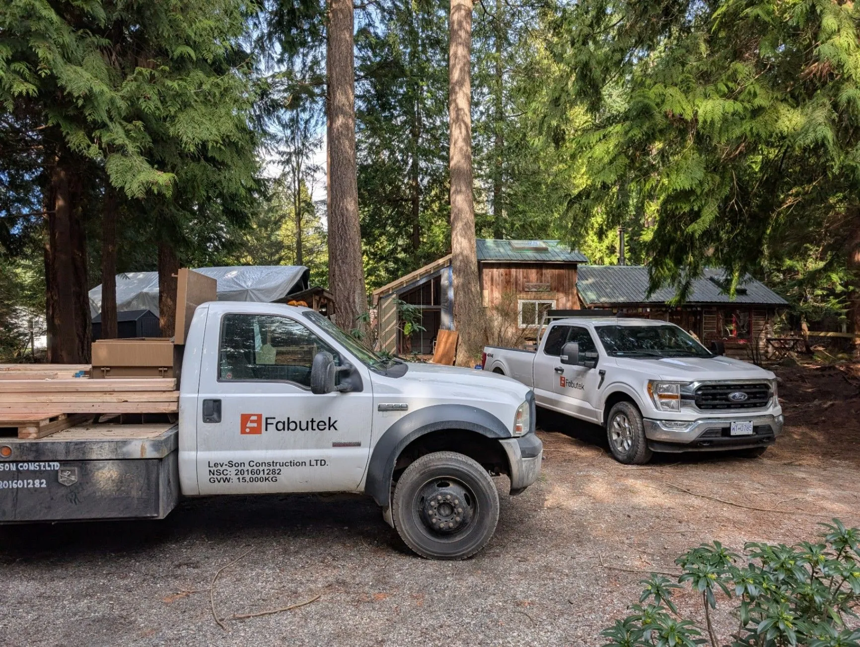 Two Fabutek-branded trucks parked at a wooded project site.